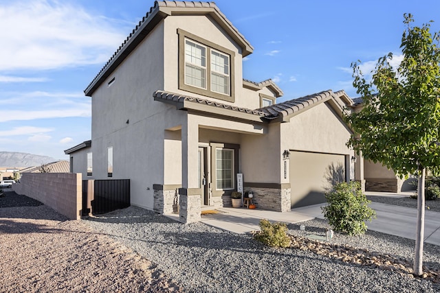 mediterranean / spanish house featuring stucco siding, stone siding, fence, a garage, and a tiled roof