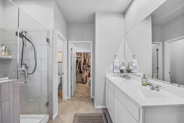 full bathroom featuring wood finished floors, double vanity, a stall shower, a sink, and toilet