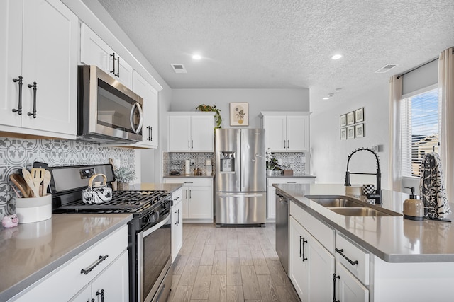 kitchen featuring light wood finished floors, visible vents, appliances with stainless steel finishes, white cabinetry, and a sink