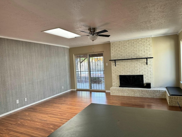 unfurnished living room featuring wood-type flooring, ceiling fan, crown molding, a brick fireplace, and a textured ceiling