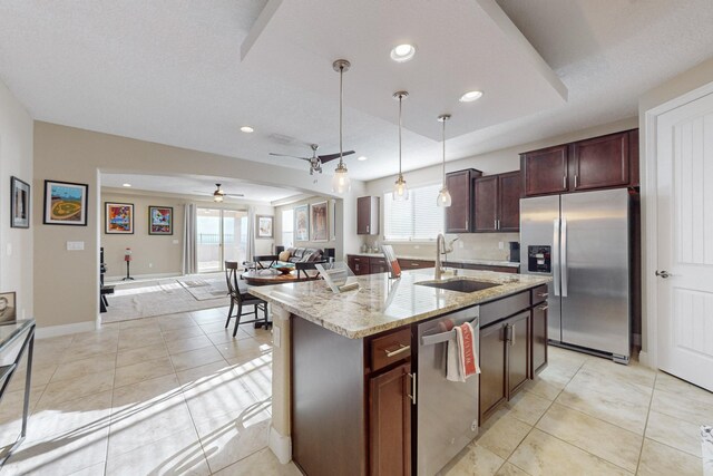 kitchen with sink, hanging light fixtures, appliances with stainless steel finishes, an island with sink, and light stone countertops