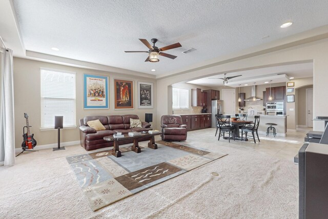 living room featuring ceiling fan, light carpet, and a textured ceiling