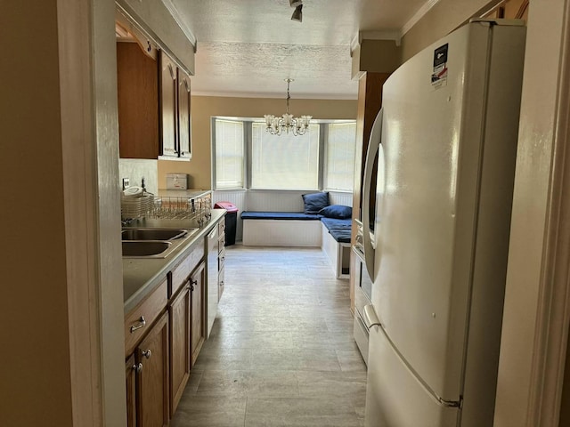 kitchen with sink, an inviting chandelier, white refrigerator, crown molding, and pendant lighting