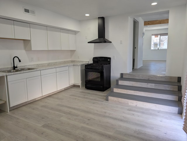 kitchen with a sink, gas stove, light wood-style floors, wall chimney exhaust hood, and white cabinets