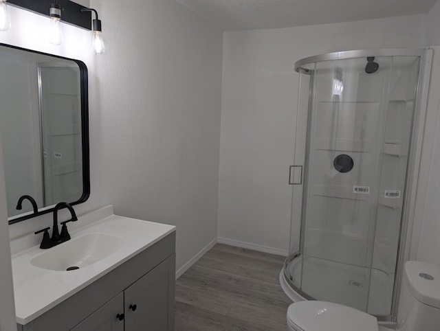 full bathroom with a shower stall, baseboards, toilet, wood finished floors, and vanity