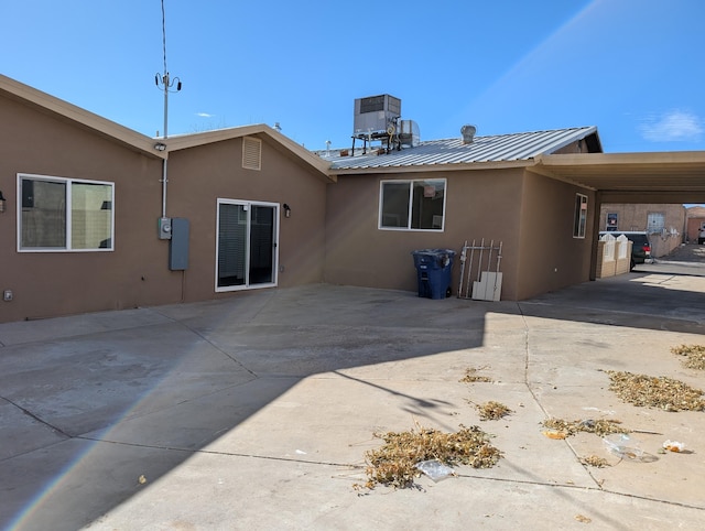 rear view of property with a carport, central air condition unit, stucco siding, and metal roof