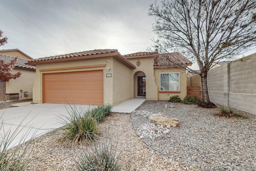 mediterranean / spanish house featuring fence, driveway, a tiled roof, and stucco siding