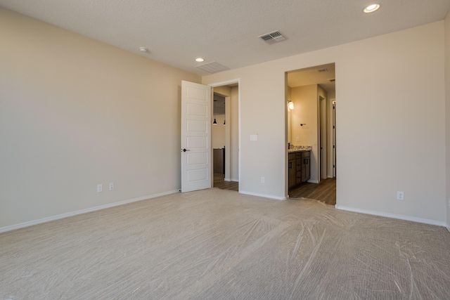 unfurnished bedroom featuring light carpet, ensuite bath, and a textured ceiling