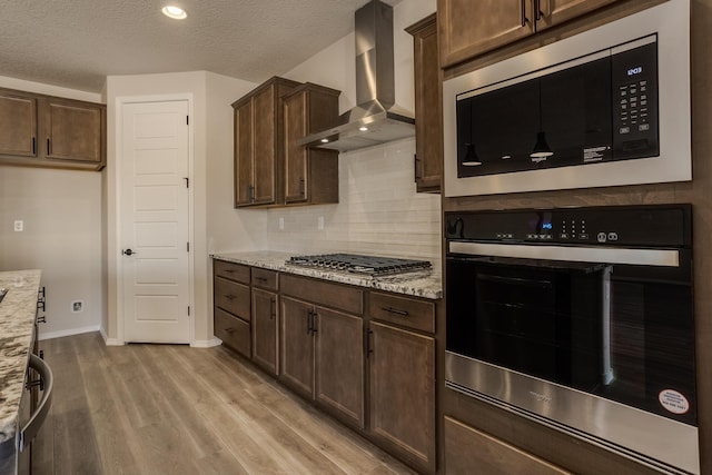 kitchen featuring light hardwood / wood-style floors, light stone counters, stainless steel appliances, a textured ceiling, and wall chimney exhaust hood