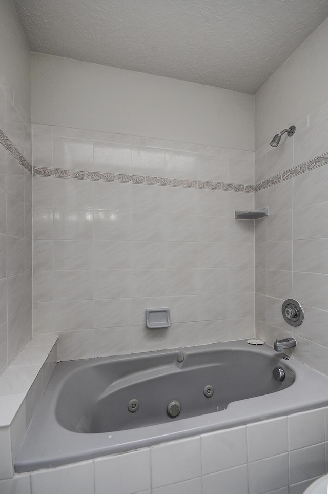 bathroom with a textured ceiling and tiled shower / bath