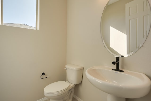 half bathroom with baseboards, a sink, and toilet