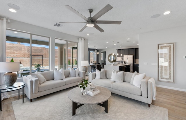 living room with ceiling fan, a textured ceiling, and light hardwood / wood-style flooring