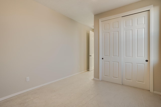 unfurnished bedroom with a closet, light colored carpet, and baseboards