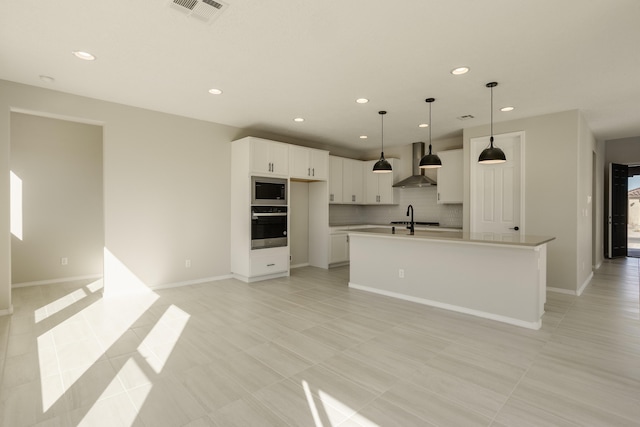 kitchen with visible vents, backsplash, appliances with stainless steel finishes, a sink, and wall chimney exhaust hood