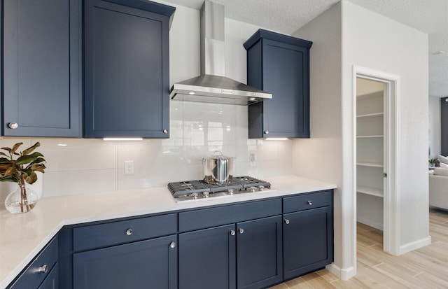 kitchen with decorative backsplash, light wood-type flooring, wall chimney exhaust hood, blue cabinets, and stainless steel gas cooktop