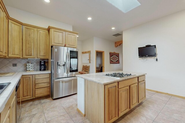 kitchen featuring a skylight, a center island, backsplash, light tile patterned floors, and appliances with stainless steel finishes