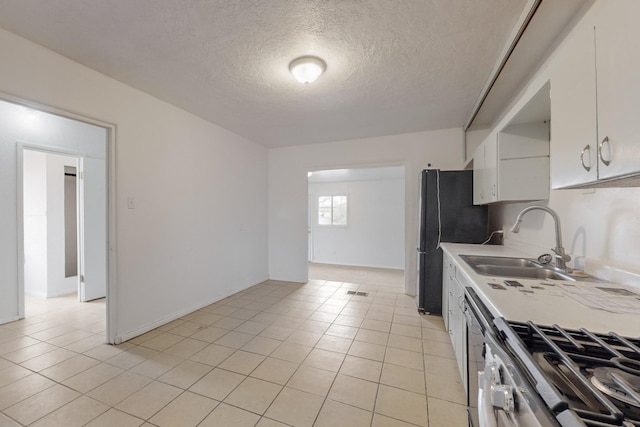 kitchen with black refrigerator, sink, light tile patterned floors, white cabinets, and range