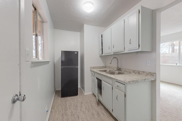 kitchen with white cabinetry, black fridge, and sink