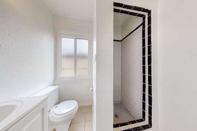 bathroom with toilet, vanity, tiled shower, and tile patterned floors