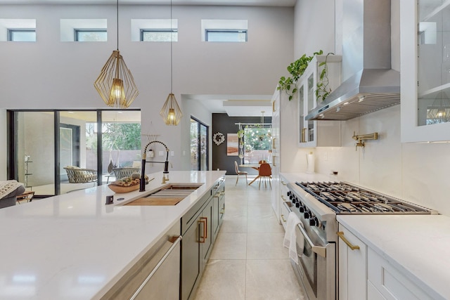 kitchen featuring high end stainless steel range oven, sink, wall chimney range hood, decorative light fixtures, and white cabinets