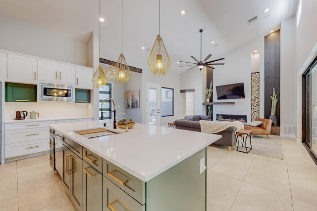 kitchen featuring stainless steel microwave, high vaulted ceiling, a center island with sink, sink, and white cabinetry