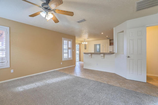 unfurnished living room featuring light tile patterned floors, ceiling fan with notable chandelier, and a textured ceiling