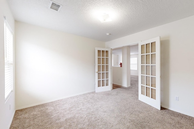 empty room with a textured ceiling, light carpet, and french doors