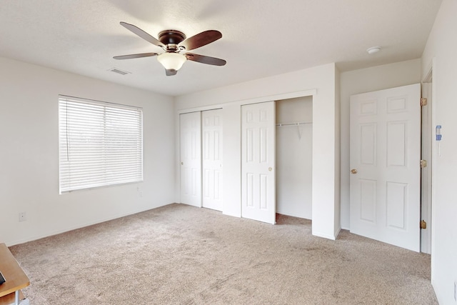 unfurnished bedroom featuring carpet, ceiling fan, and multiple closets