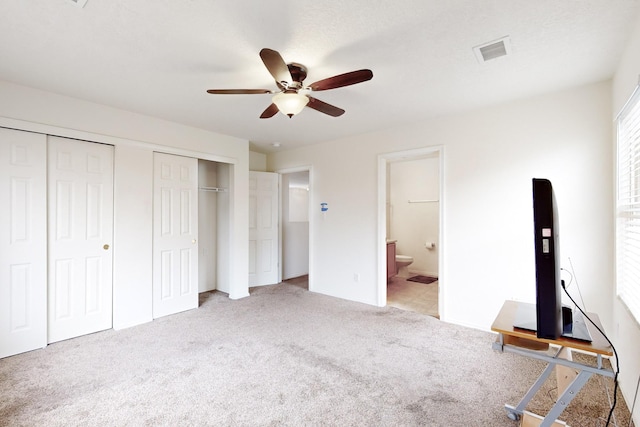 unfurnished bedroom featuring ceiling fan, light colored carpet, two closets, and ensuite bath