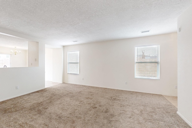 unfurnished room featuring a notable chandelier, a textured ceiling, and light carpet