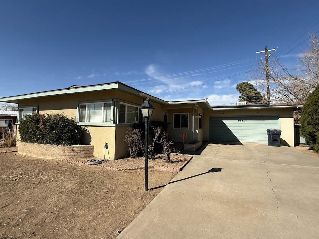 ranch-style house with a garage, concrete driveway, and stucco siding