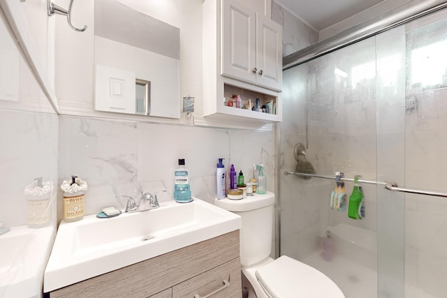 bathroom with a shower with door, vanity, backsplash, toilet, and tile walls