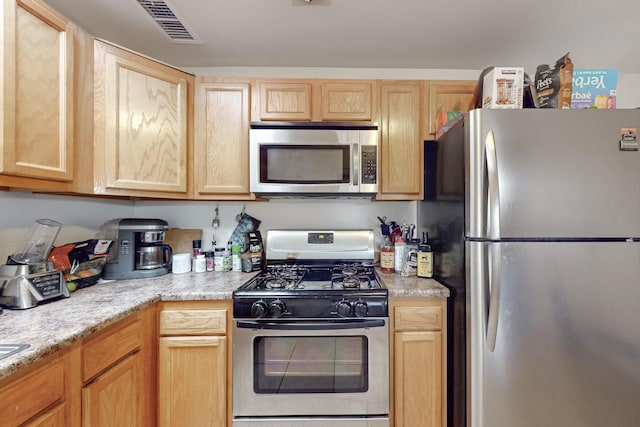 kitchen featuring light stone counters, light brown cabinets, and stainless steel appliances