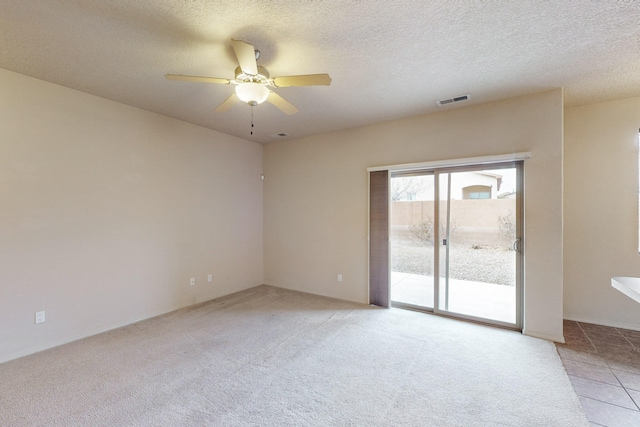 spare room with a textured ceiling, light colored carpet, and ceiling fan