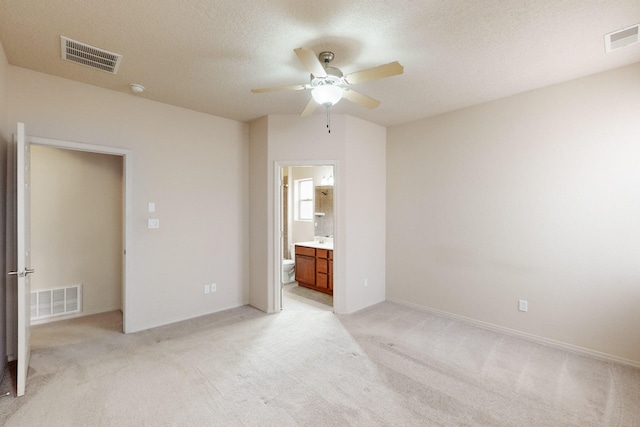 unfurnished bedroom featuring ensuite bath, ceiling fan, light carpet, and a textured ceiling