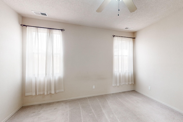 spare room featuring light carpet, a textured ceiling, ceiling fan, and a healthy amount of sunlight