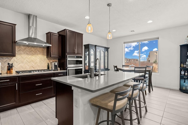 kitchen featuring light tile patterned floors, stainless steel appliances, a center island with sink, and wall chimney exhaust hood