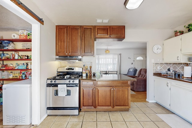 kitchen featuring light tile patterned floors, a barn door, backsplash, and gas stove