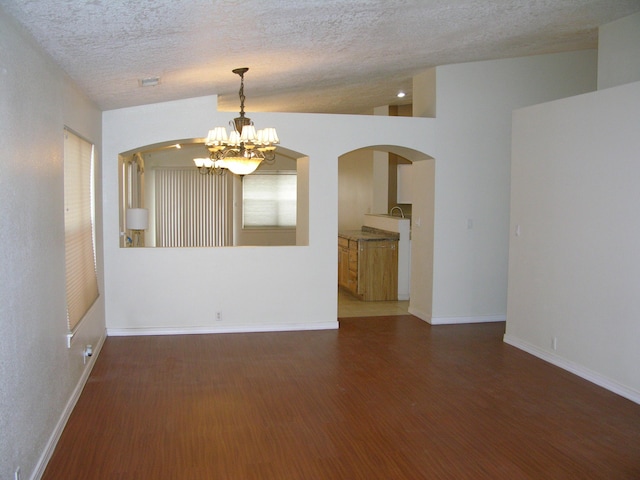 unfurnished room featuring a chandelier, lofted ceiling, a textured ceiling, and dark wood-type flooring