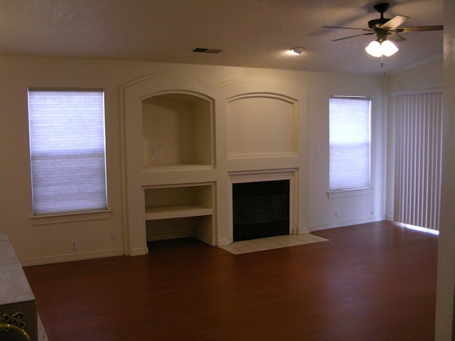 unfurnished living room featuring a textured ceiling, built in features, ceiling fan, and dark wood-type flooring