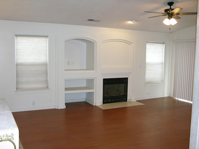 unfurnished living room featuring built in shelves, ceiling fan, dark hardwood / wood-style floors, lofted ceiling, and a textured ceiling