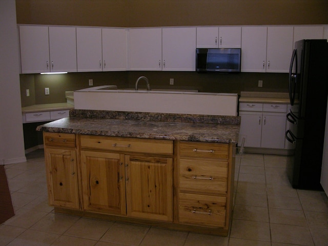 kitchen with black refrigerator, light tile patterned floors, a center island, and white cabinetry