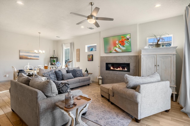 living room with a tile fireplace and ceiling fan with notable chandelier