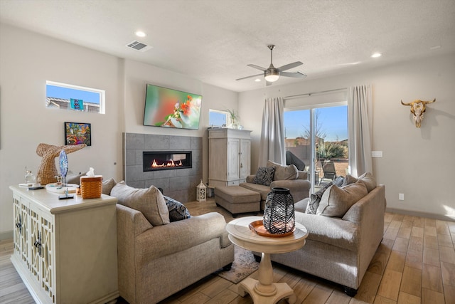 living room with a tiled fireplace, ceiling fan, light hardwood / wood-style flooring, and a textured ceiling