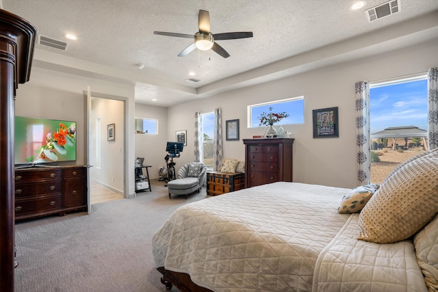 bedroom with light colored carpet, ceiling fan, a textured ceiling, and a tray ceiling