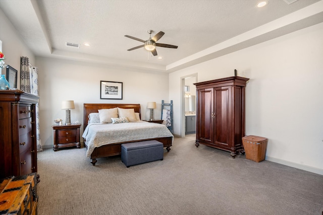 bedroom with a textured ceiling, a raised ceiling, connected bathroom, ceiling fan, and light carpet