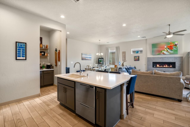 kitchen with a textured ceiling, a tile fireplace, a center island with sink, ceiling fan with notable chandelier, and sink