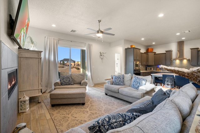 living room with a textured ceiling, ceiling fan, and light hardwood / wood-style flooring