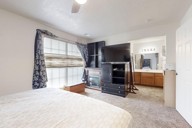 carpeted bedroom with ensuite bathroom, ceiling fan, and a textured ceiling