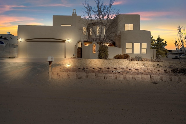 pueblo-style house with a garage, driveway, and stucco siding